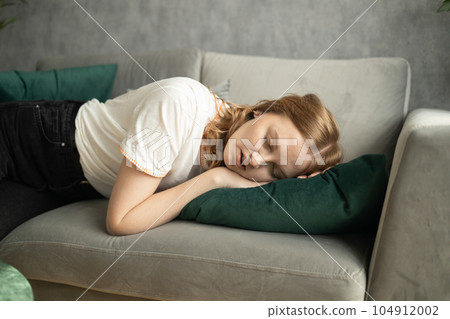 Sleeping blonde tired woman taking nap on the sofa during the day  104912002