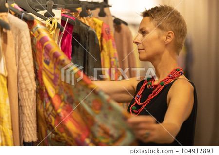 Adult stylish woman looking over the colorful clothes at the boutique Adult stylish woman looking over the colorful clothes at the boutique 104912891