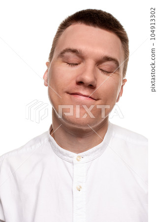 Charming handsome young man in a white shirt is making faces, while standing isolated on a white background Charming handsome young man in a white shirt is making faces, while standing isolated on a white background 104913302