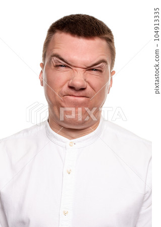 Charming handsome young man in a white shirt is making faces, while standing isolated on a white background 104913335