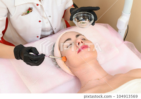 The cosmetologist applies a liquid gel to the face with a wide brush The cosmetologist applies a liquid gel to the face with a wide brush 104913569
