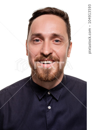Portrait of a handsome, unshaven man, dressed in a dark blue shirt, standing against a white background. Self confident man. 104913593