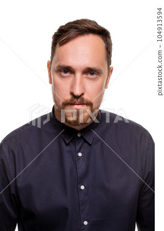Portrait of a handsome, unshaven man, dressed in a dark blue shirt, standing against a white background. Self confident man. 104913594