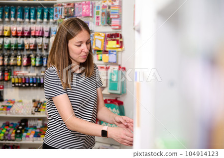 Pleasant female seller in office supply shop, stacking school supplies on display shelves, working on merchandising Pleasant female seller in office supply shop, stacking school supplies on display shelves, working on merchandising 104914123