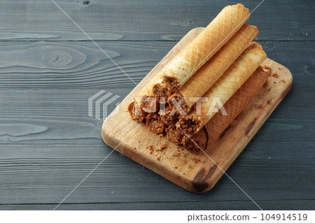 Waffle tubes with chocolate filling on wooden board Waffle tubes with chocolate filling on wooden board 104914519