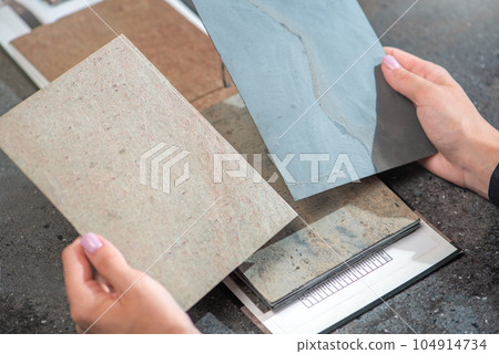 Architect hand choosing sample of stone material or tile texture collection on the table in studio. Designer working for interior architecture and furniture design project. 104914734