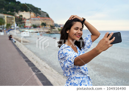 Beautiful smiling young woman takes selfie at the Promenade des Anglais in Nice, France 104916490