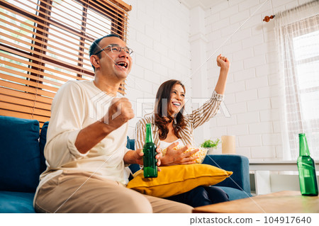 Couple of happy husband and wife watching sports match together Couple of happy husband and wife watching sports match together 104917640