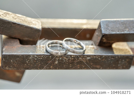 Two hands with wedding rings rest on a strong anchor chain 104918271