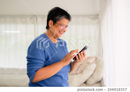 Healthy mature woman holding smartphone using mobile app and chatting with friends, Senior people with technology at home, Grandmother relaxing at home with happiness 104918357