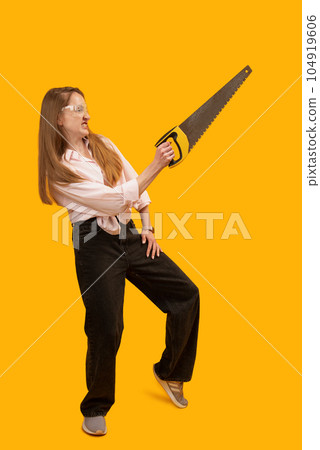 Smiling young woman wearing goggles and holding hand saw. Isolated on yellow background. Vertical frame. Copy space. 104919606