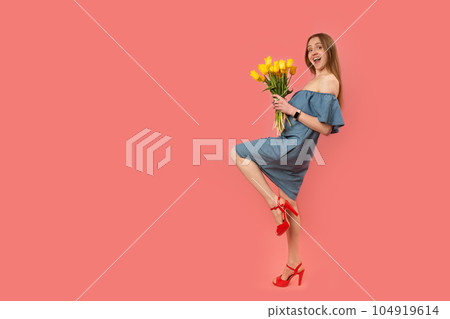 Happy beautiful young woman in gray sundress and red sandals posing in studio with bouquet of tulips. Isolated on pink background. Copy space. Happy beautiful young woman in gray sundress and red sandals posing in studio with bouquet of tulips. Isolated on pink background. Copy space. 104919614