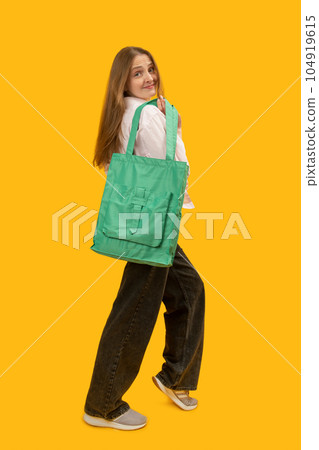 Full-leight portrait of young woman with green textile shopping bag. Studio photo on yellow background. Vertical frame. Full-leight portrait of young woman with green textile shopping bag. Studio photo on yellow background. Vertical frame. 104919615