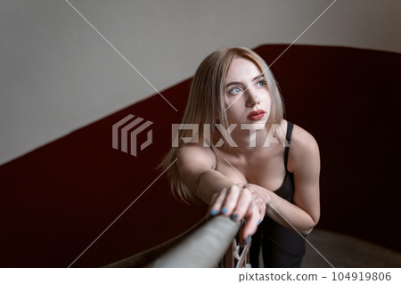 Portrait of young fair-haired woman in top with deep neckline inside. Model poses for photo indoor. 104919806