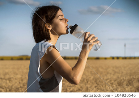 Girl drinks water from a bottle during her training. 104920546