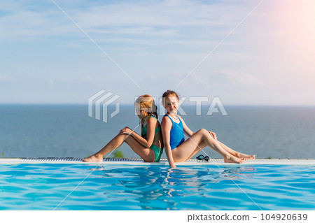 Two teenage girls sitting on the side of the pool 104920639