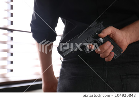 Man with gun near window indoors, closeup Man with gun near window indoors, closeup 104920848