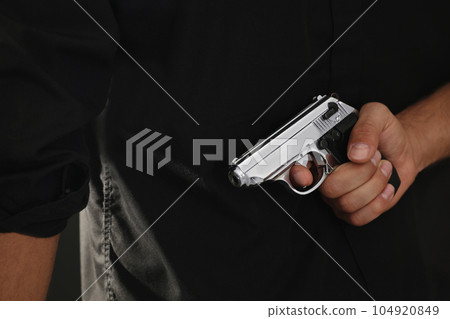 Professional killer with gun on black background, closeup Professional killer with gun on black background, closeup 104920849