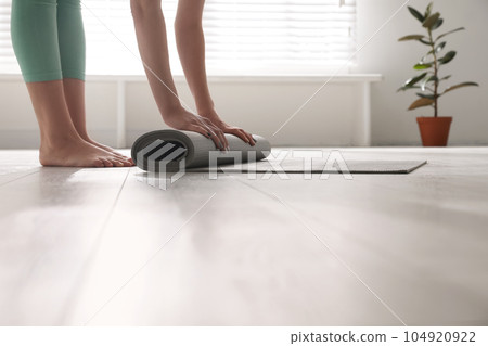 Woman rolling her mat on floor in yoga studio, closeup 104920922