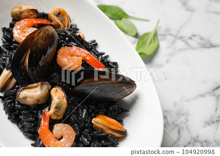 Delicious black risotto with seafood on white marble table, closeup Delicious black risotto with seafood on white marble table, closeup 104920998