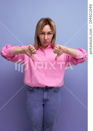young sad blond caucasian woman with loose straight hair dressed in a pink blouse and jeans shows 104921049