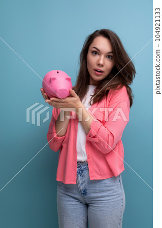 positive brunette young woman in a shirt and jeans holding a piggy bank with savings positive brunette young woman in a shirt and jeans holding a piggy bank with savings 104921133