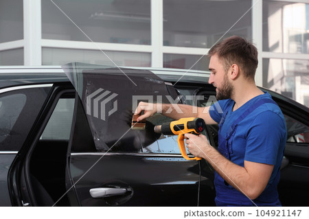 Worker tinting car window with heat gun in workshop 104921147