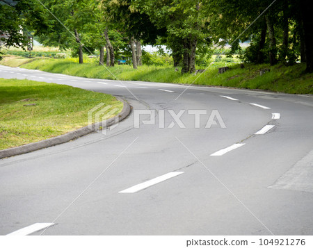 一條彎曲的單車道道路,中心線為白色虛線。 一條彎曲的單車道道路,中心線為白色虛線。 104921276