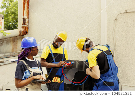 Smiling technicians happy with freon levels in outdoor air conditioner while using manifold gauges to accurately measure HVAC system pressure, ensuring optimal cooling performance and efficiency Smiling technicians happy with freon levels in outdoor air conditioner while using manifold gauges to accurately measure HVAC system pressure, ensuring optimal cooling performance and efficiency 104921531