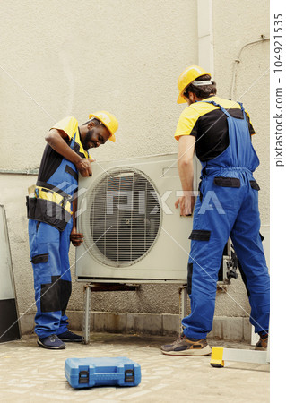 Professional worker and licensed serviceman taking apart old unfunctional condenser to replace it with new performant air conditioner after draining refrigerant and replacing ductwork Professional worker and licensed serviceman taking apart old unfunctional condenser to replace it with new performant air conditioner after draining refrigerant and replacing ductwork 104921535