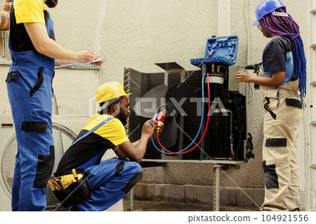 Adept repairman expertly refilling freon in HVAC system while using benchmarking tools to precisely measure the pressure in air conditioner, ensuring optimal cooling performance Adept repairman expertly refilling freon in HVAC system while using benchmarking tools to precisely measure the pressure in air conditioner, ensuring optimal cooling performance 104921556