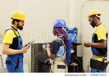 Professional workers contracted by customer to search for refrigerant leaks on external hvac system evaporator coil leading to poor cooling problems during hot summer months 104921613