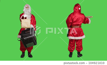 Deliveryman in red santa suit carrying backpack with pizza box and paper bag order, christmas eve delivery concept. Young man saint nick character against full body greenscreen backdrop. Deliveryman in red santa suit carrying backpack with pizza box and paper bag order, christmas eve delivery concept. Young man saint nick character against full body greenscreen backdrop. 104921810