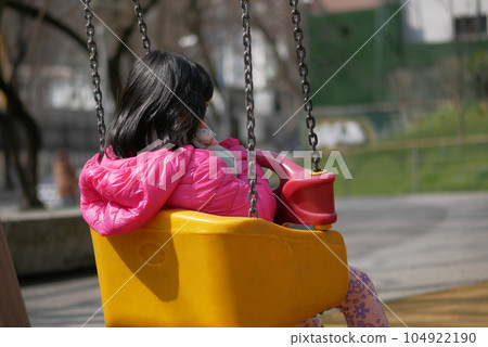 child having fun on a swing on the playground in public park. 104922190
