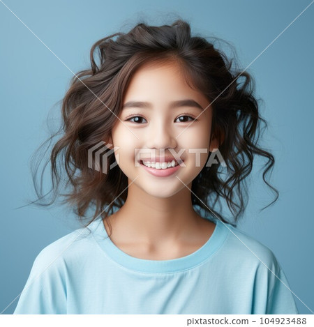 Portrait of a smiling Asian little girl with black hair on a blue background. Happy small Asian kid with a smile and long wavy hair. Cheerful white female child in a blue shirt with shiny white teeth. Portrait of a smiling Asian little girl with black hair on a blue background. Happy small Asian kid with a smile and long wavy hair. Cheerful white female child in a blue shirt with shiny white teeth. 104923488