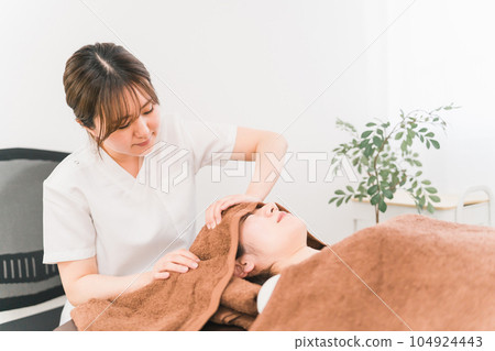 A woman who receives a head / scalp massage at a chiropractic clinic and a therapist, a chiropractor, a masseuse (manipulative clinic / salon) 104924443