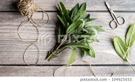 Bunch of green sage leaves on gray wooden table, herbs scissors string flat lay, overhead view 104925033