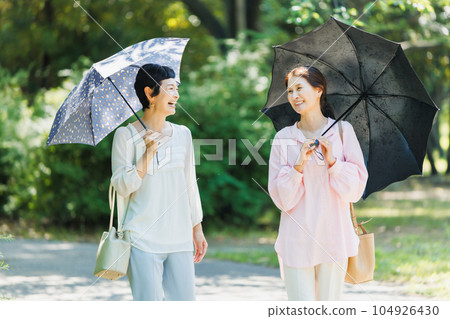 一位中年婦女撐著陽傘在公園裡散步 104926430