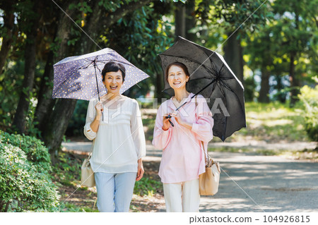 一位中年婦女撐著陽傘在公園裡散步 一位中年婦女撐著陽傘在公園裡散步 104926815