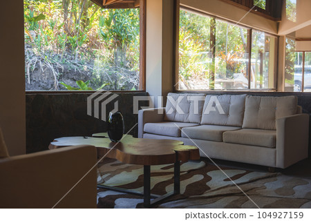 Luxury modern hotel interior design with sofa and armchair overlooking beautiful nature from glass window. Luxury travel vacation concept Luxury modern hotel interior design with sofa and armchair overlooking beautiful nature from glass window. Luxury travel vacation concept 104927159