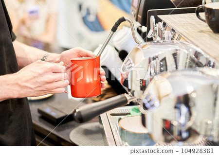 Barista pours cream into the cup of coffee. A small coffee business. A professional barista prepares coffee in a carob coffee machine. Favorite job in the restaurant industry. Barista pours cream into the cup of coffee. A small coffee business. A professional barista prepares coffee in a carob coffee machine. Favorite job in the restaurant industry. 104928381