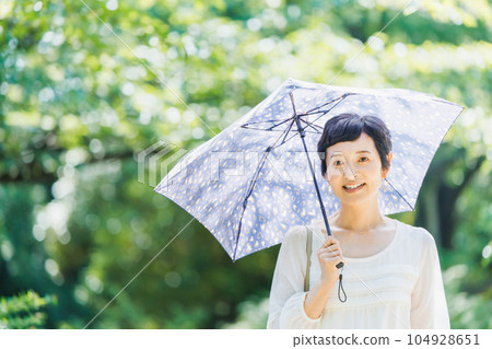 一位中年婦女撐著陽傘在公園裡散步 一位中年婦女撐著陽傘在公園裡散步 104928651