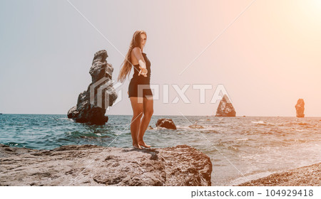 Woman summer travel sea. Happy tourist in hat enjoy taking picture outdoors for memories. Woman traveler posing on the beach at sea surrounded by volcanic mountains, sharing travel adventure journey 104929418
