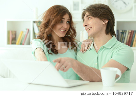 Portrait of smiling young couple pointing at laptop at home Portrait of smiling young couple pointing at laptop at home 104929717