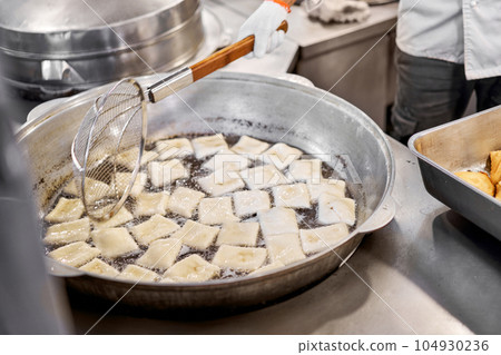 street cafe. Male cook preparing delicious National Kazakh pastries baursak. . Fry dough in boiling oil in a frying pan. 104930236