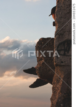 Vertical shot of a guy in a cap sitting on a stone surface admiring the sky Vertical shot of a guy in a cap sitting on a stone surface admiring the sky 104931475