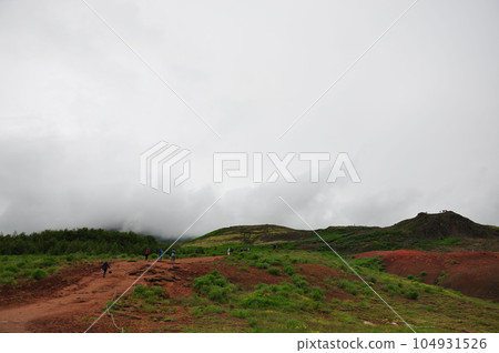 Aerial view of people climbing up a foggy mountain near Kerid Crater in Iceland 104931526