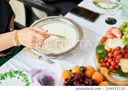 Making cheese from goat milk at home. Female and stir cheese sourdough with a spoon in a saucepan. Technology of cooking cheese. Cheese-making processes. Cooking concept 104933120