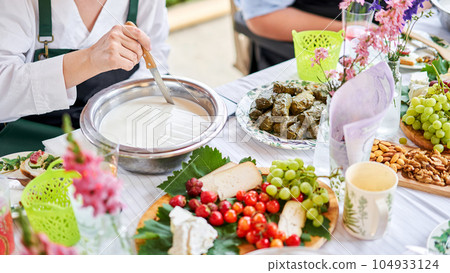 Cut with a knife, separate the serum. Master class and cheese tasting. Women make cheese. The enzyme and starter culture are added to the milk in a metal container. Milk folding process, home Cut with a knife, separate the serum. Master class and cheese tasting. Women make cheese. The enzyme and starter culture are added to the milk in a metal container. Milk folding process, home 104933124