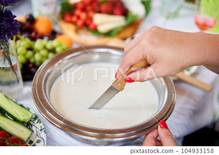 Cut with a knife, separate the serum. Master class and cheese tasting. Women make cheese. The enzyme and starter culture are added to the milk in a metal container. Milk folding process, home 104933158